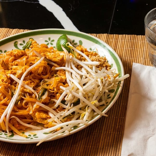 A plate of Pad Thai noodles with bean sprouts, lime, and peanuts, next to a glass of water.