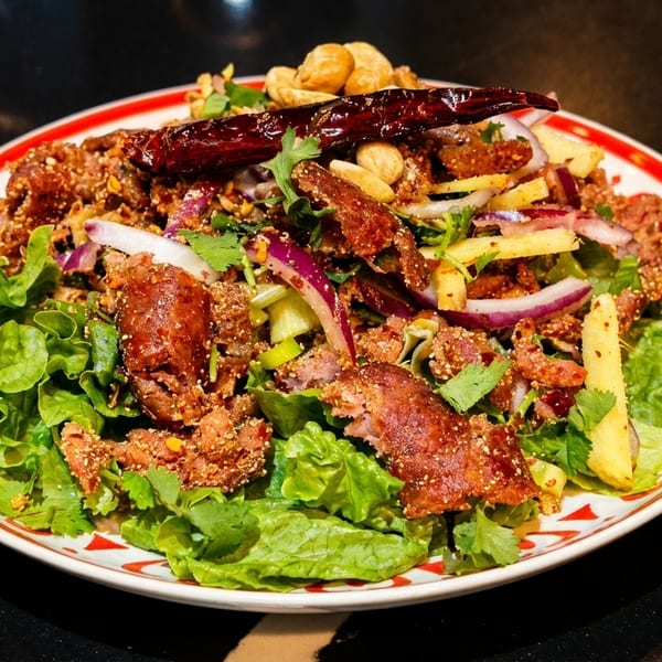 Spicy Thai salad with crispy pork, red onion, cashews, and dried chilies on a bed of lettuce.