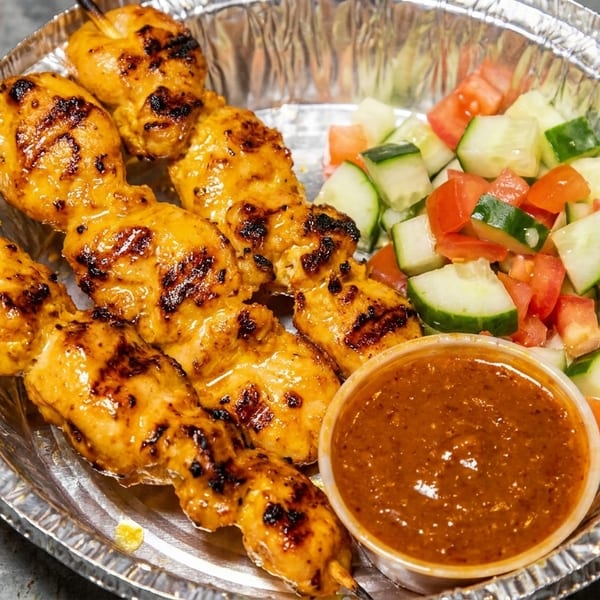 Grilled chicken satay skewers with peanut sauce and a side of cucumber and tomato salad.