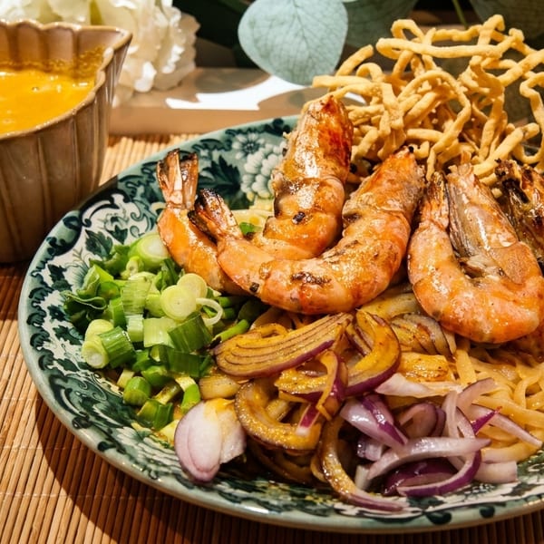 Khao Soi with grilled prawns, crispy noodles, red onions, and scallions, served with curry sauce.