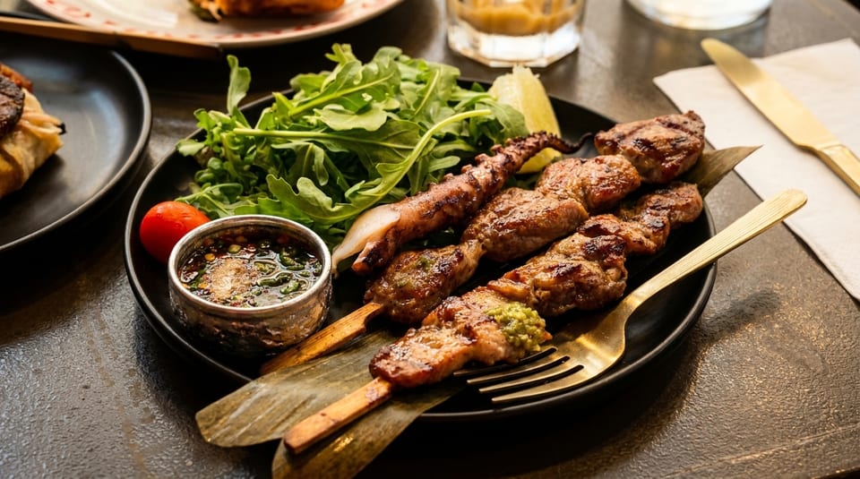 Grilled skewers of meat and squid, with a side of arugula, tomato, lime, and dipping sauce.