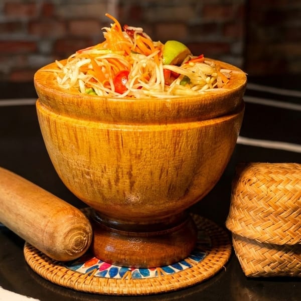 Som Tum (papaya salad) in a wooden mortar with a pestle and a woven basket.